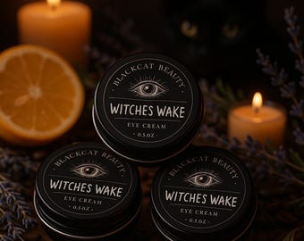May include: Three black tins of "Witches Wake" eye cream are stacked, with the text "BLACKCAT BEAUTY" and an eye graphic. The background includes a lit candle, a lemon slice, and a black cat. The eye cream is 0.5 oz.