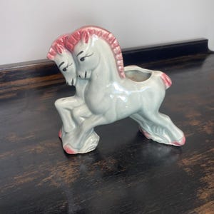 May include: A white ceramic mug with a black handle and the text "But First, Coffee" in a black, handwritten-style font. The mug is on a white surface.