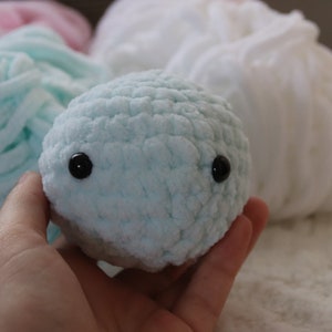 May include: A light blue crocheted stuffed animal with black button eyes. The animal is being held in a hand.