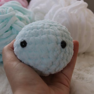 May include: A light blue crocheted stuffed animal with black eyes. The animal is being held in a hand.