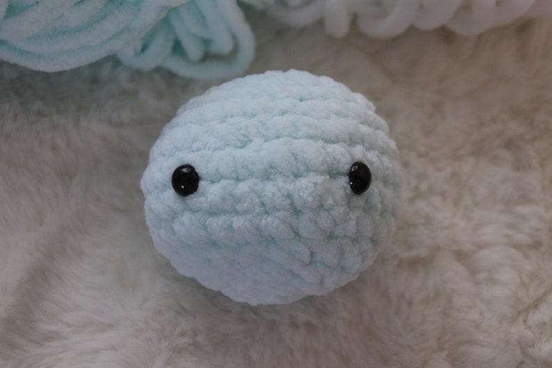 May include: A light blue crocheted plush toy with black button eyes.