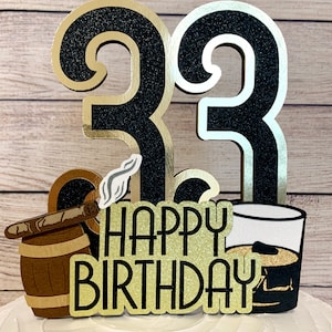 May include: Black and gold glitter cake topper with the number 33, a cigar in a barrel, a glass of whiskey, and the text "Happy Birthday".