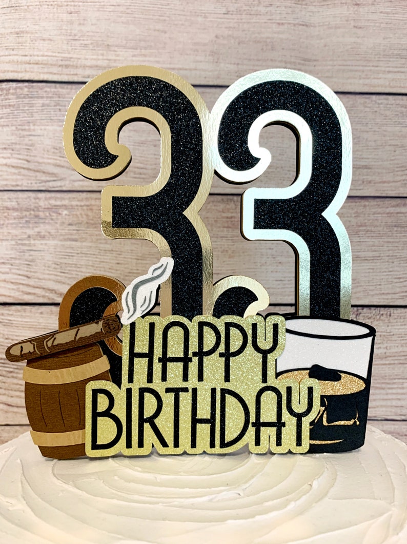 May include: Black and gold glitter cake topper with the number 33, a cigar in a barrel, a glass of whiskey, and the text "Happy Birthday".