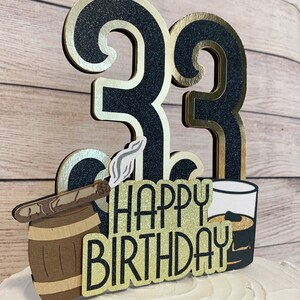 May include: Black and gold glitter cake topper with the numbers 33, a barrel with a cigar, a glass of whiskey, and the text "Happy Birthday".