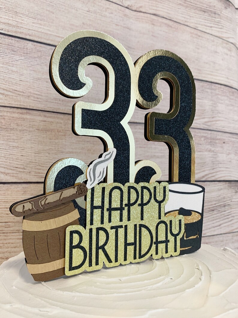May include: Black and gold glitter cake topper with the numbers 33, a barrel with a cigar, a glass of whiskey, and the text "Happy Birthday".