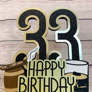 May include: Black and gold glitter cake topper with the number 33, a cigar in a barrel, a glass of whiskey, and the text "Happy Birthday".
