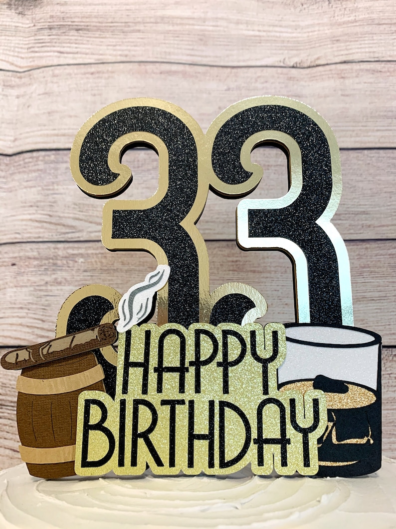 May include: Black and gold glitter cake topper with the number 33, a cigar in a barrel, a glass of whiskey, and the text "Happy Birthday".
