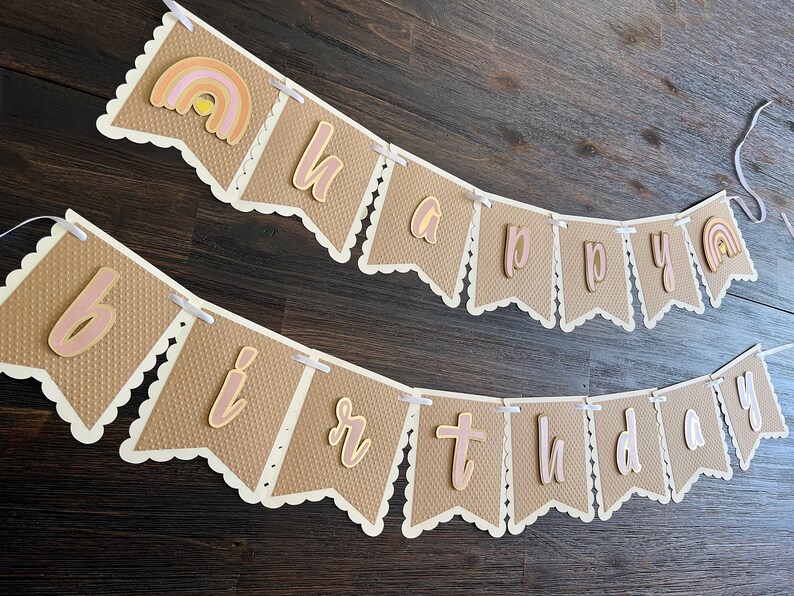 May include: A brown and white banner with the words "happy birthday" in pink and gold letters. The banner has a scalloped edge and is decorated with small rainbows.