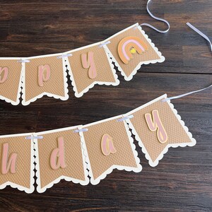 May include: A brown and white banner with the word "Happy" and a rainbow design. The banner is strung with white ribbon.