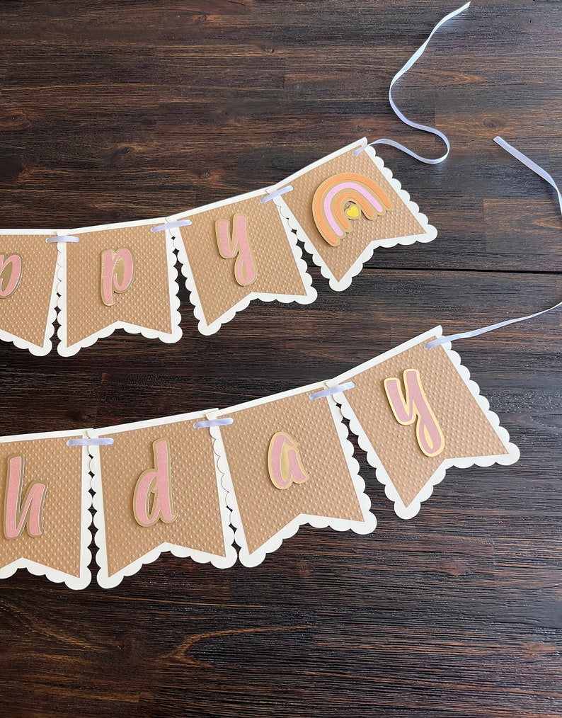 May include: A brown and white banner with the word "Happy" and a rainbow design. The banner is strung with white ribbon.
