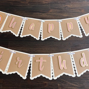 May include: A brown paper banner with white scalloped edges and pink letters that spell out "happy birthday".
