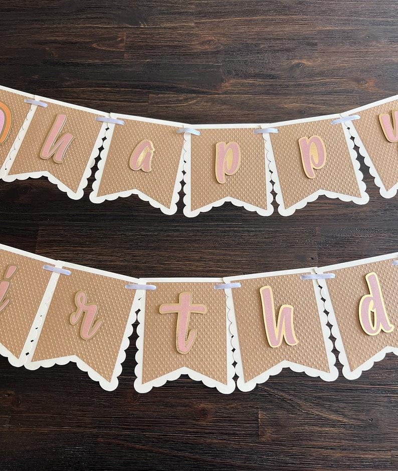 May include: A brown paper banner with white scalloped edges and pink letters that spell out "happy birthday".