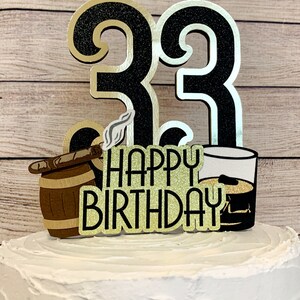 May include: Black and gold glitter cake topper with the number 33, a barrel with a cigar, a glass of whiskey, and the words "Happy Birthday".