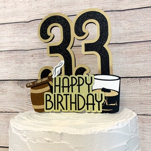 May include: Black and gold glitter cake topper with the numbers 33, a barrel with a cigar, a glass of whiskey, and the text "Happy Birthday".