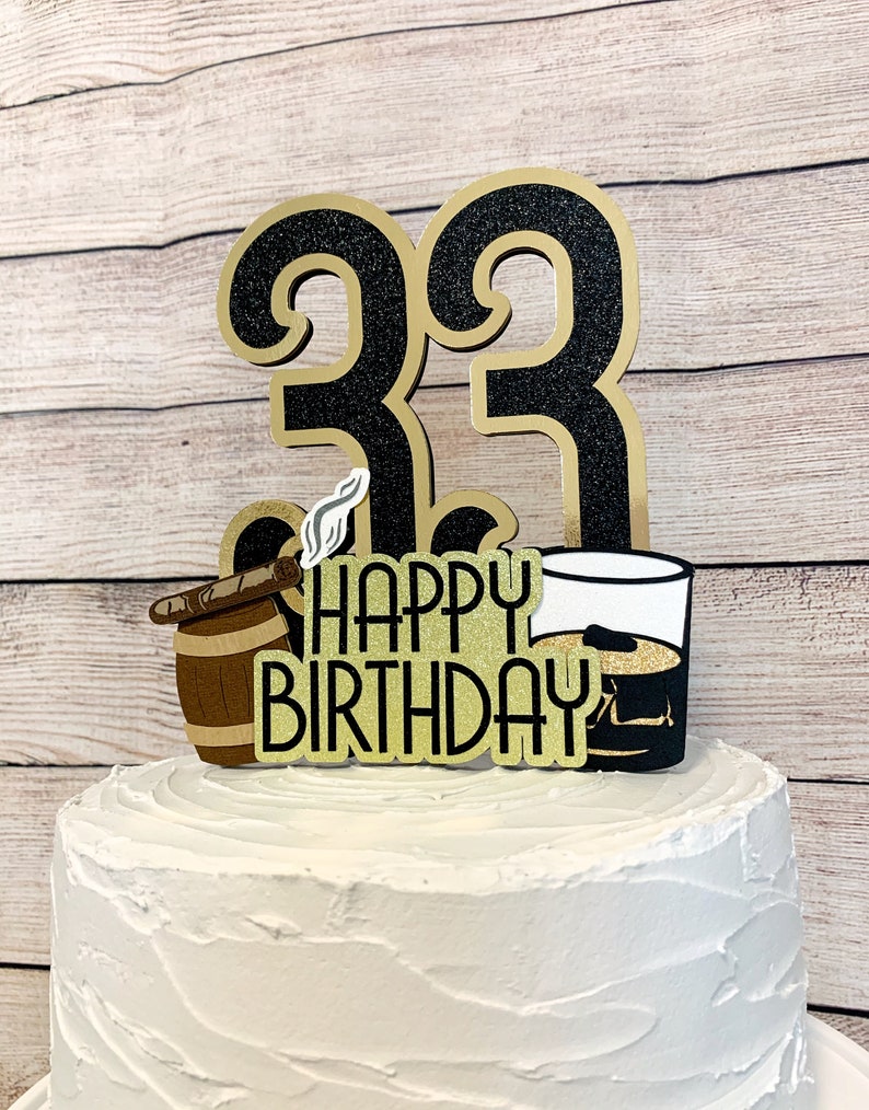 May include: Black and gold glitter cake topper with the numbers 33, a barrel with a cigar, a glass of whiskey, and the text "Happy Birthday".