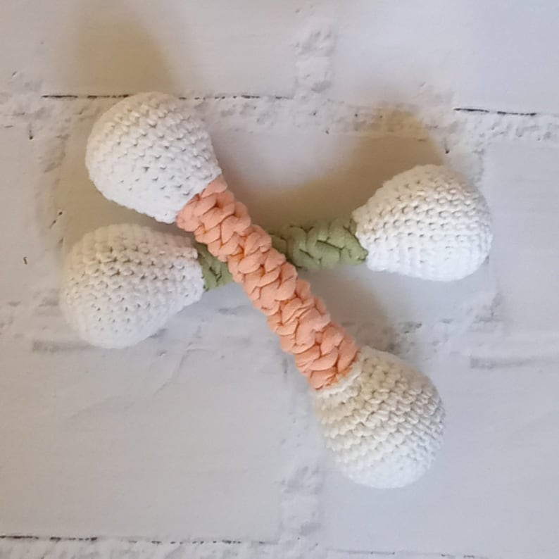 May include: Two crocheted dog toys in the shape of bones. The bones are white with peach and green accents.