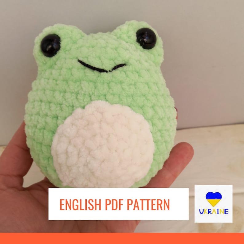 Może przedstawiać: Wz&oacute;r na szydełku do amigurumi zielonej i białej żaby. Wz&oacute;r jest dostępny jako plik PDF do pobrania. Obraz zawiera tekst "ENGLISH PDF PATTERN" i serce w kolorach flagi ukraińskiej.