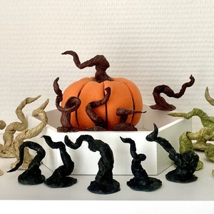 May include: A collection of 10 handmade felt pumpkin stem decorations in various colours, including brown, green, and beige. The stems are arranged around a felt pumpkin.
