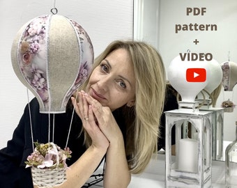 Puede incluir: Una mujer sostiene un globo aerostático artesanal con un patrón floral. El globo está hecho de tela y tiene una cesta con flores. El texto "PDF pattern + VIDEO" es visible en la imagen.