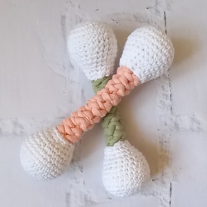 May include: Two crocheted rattle toys with white balls and multi-colored handles. The handles are made of a peach colored yarn and a green yarn.