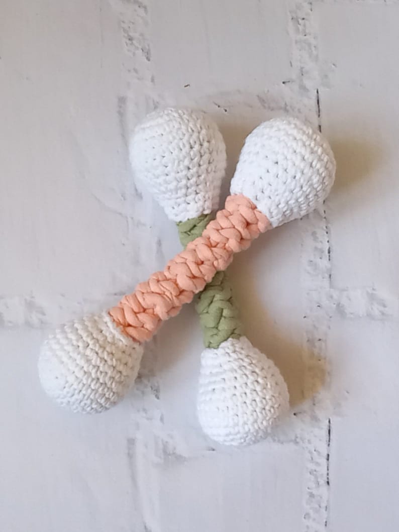 May include: Two crocheted rattle toys with white balls and multi-colored handles. The handles are made of a peach colored yarn and a green yarn.