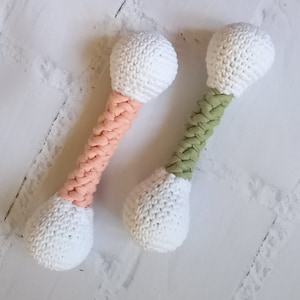 May include: Two crocheted toy dumbbells, one with a pink handle and one with a green handle. Both dumbbells have white crocheted ends.