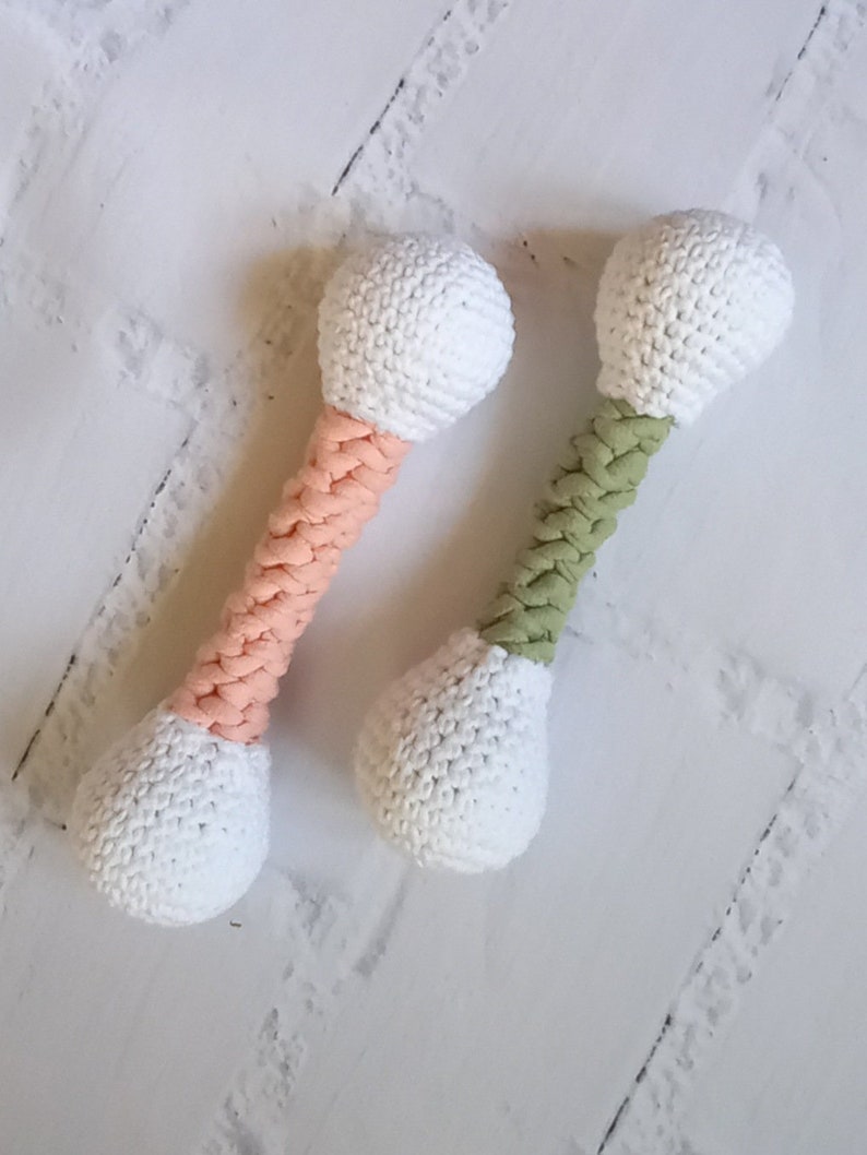 May include: Two crocheted toy dumbbells, one with a pink handle and one with a green handle. Both dumbbells have white crocheted ends.