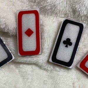 May include: Four white rectangular tiles with black and red borders. Each tile features a different playing card suit: spades, diamonds, clubs, and hearts.
