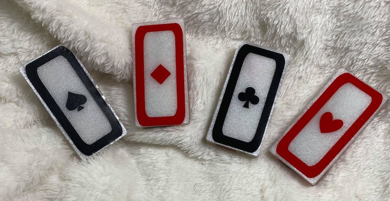 May include: Four white rectangular tiles with black and red borders. Each tile features a different playing card suit: spades, diamonds, clubs, and hearts.