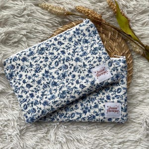 Peut inclure: Deux pochettes zippées blanches avec un motif floral bleu et le texte "June Flower" sur chacune.