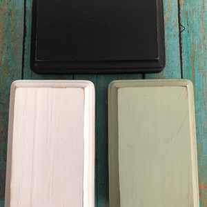 May include: Three wooden boxes with different paint finishes. The top box is black, the middle box is white, and the bottom box is a light green.