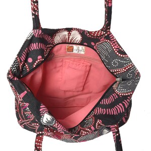 May include: Open tote bag with a black background and a pink and white floral pattern. The interior is a solid pink color with a small pocket. The bag has two handles and a zipper closure. The tag says "Gorjus".
