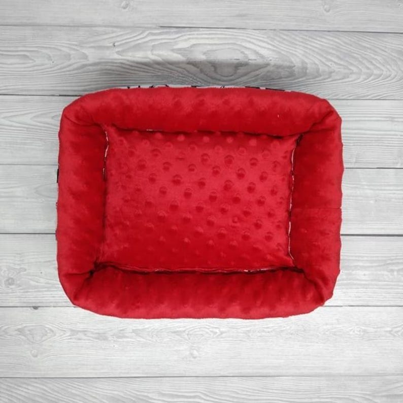 K&ouml;nnte beinhalten: Rotes Haustierbett mit erh&ouml;htem Rand und weicher, strukturierter Auskleidung. Das Bett ist mit einem pl&uuml;schigen, roten Kissen gef&uuml;llt.