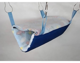 May include: A blue and white hanging hammock bed for small pets. The bed is made of soft fabric and has a blue outer layer with a white and pink patterned inner layer. The bed is suspended by two blue straps with metal hooks.