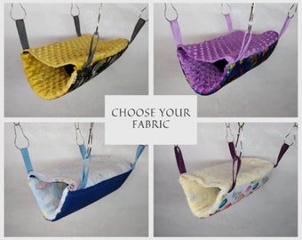 May include: Four different fabric options for a small pet hammock. The hammocks are made of soft, colorful fabrics with a variety of patterns. The hammocks are suspended from the ceiling with two metal hooks.