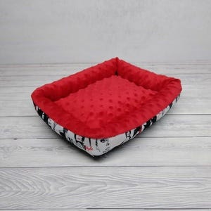 K&ouml;nnte beinhalten: Rotes und wei&szlig;es Hundebett mit einem schwarz-wei&szlig;en Druck von Gesichtern und dem Wort "Style".