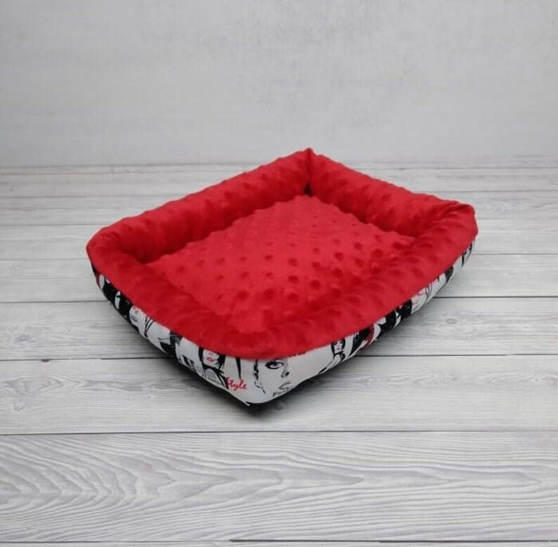 K&ouml;nnte beinhalten: Rotes und wei&szlig;es Hundebett mit einem schwarz-wei&szlig;en Druck von Gesichtern und dem Wort "Style".