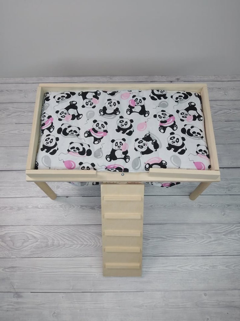 Peut inclure: Un lit pour animal domestique en bois avec une rampe et un rev&ecirc;tement en tissu amovible &agrave; imprim&eacute; panda. Le rev&ecirc;tement est blanc avec des pandas noirs et blancs tenant des ballons roses.
