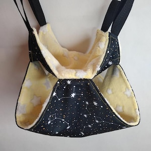 May include: A black and yellow hanging pet bed with a white star pattern and constellations. The bed is lined with soft, white fleece.