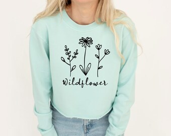 May include: A light blue cropped sweatshirt with a black graphic of three stylized wildflowers and the word "Wildflower" printed on the front.