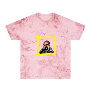 May include: Pink tie-dye t-shirt featuring a graphic of a person with a red beanie and glasses, framed in a yellow square. The person is holding their hands up to their face. The shirt has a crew neck and short sleeves.
