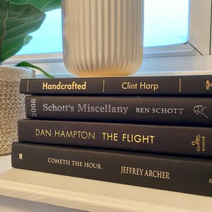 Może przedstawiać: Stosik pięciu czarnych książek w twardej oprawie ze złotymi napisami na grzbietach. Tytuły to "Handcrafted", "Schott's Miscellany", "The Flight", "Cometh the Hour" i "Jeffrey Archer".
