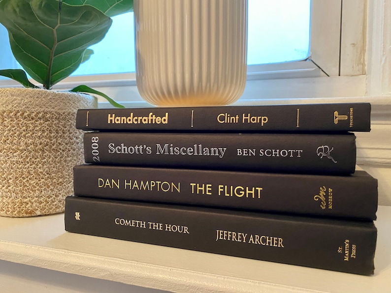 Może przedstawiać: Stosik pięciu czarnych książek w twardej oprawie ze złotymi napisami na grzbietach. Tytuły to "Handcrafted", "Schott's Miscellany", "The Flight", "Cometh the Hour" i "Jeffrey Archer".