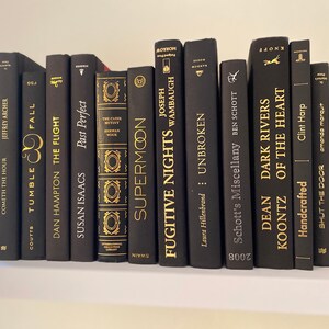 Może przedstawiać: P&oacute;łka z czarnymi książkami ze złotymi napisami. Tytuły to "Cometh the Hour", "Tumble Fall", "Fugitive Nights", "Unbroken", "Schott's Miscellany", "Dean Koontz", "Dark Rivers", "Of the Heart", "Shut the Door" i "Supermoon".