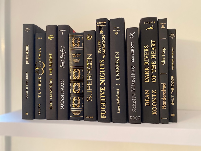 Może przedstawiać: P&oacute;łka z czarnymi książkami ze złotymi napisami. Tytuły to "Cometh the Hour", "Tumble Fall", "Fugitive Nights", "Unbroken", "Schott's Miscellany", "Dean Koontz", "Dark Rivers", "Of the Heart", "Shut the Door" i "Supermoon".