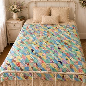 May include: A patchwork quilt featuring a repeating geometric pattern of small triangles in various pastel and floral prints, including shades of light blue, yellow, pink, and green, covering a bed with three cream-colored crocheted throw pillows.