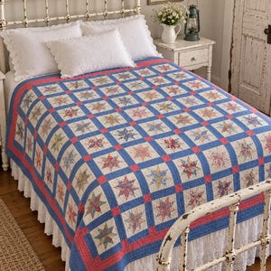 May include: A bed quilt featuring a repeating star pattern in various floral prints, set against a white background. The quilt is framed by a blue grid and a coral pink border, with white lace-trimmed pillows and a white ruffled bed skirt.