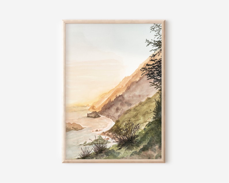 May include: A framed watercolor painting depicting a coastal landscape with a steep, grassy cliffside meeting the ocean. The scene features soft golden light, muted green and brown tones, and a silhouette of a tree on the right side.