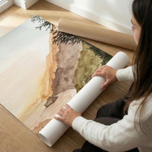 May include: A large rectangular art print featuring a watercolor landscape painting with soft beige, brown, and olive green tones. The artwork depicts abstract hills and dark tree silhouettes, partially rolled up on a white paper tube.