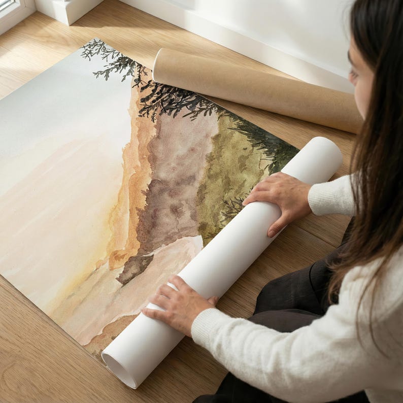 May include: A large rectangular art print featuring a watercolor landscape painting with soft beige, brown, and olive green tones. The artwork depicts abstract hills and dark tree silhouettes, partially rolled up on a white paper tube.